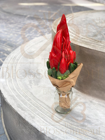Sculptural red capsicum and chili bouquet in a glass jar with green vegetables, wrapped in brown craft paper and photographed on urban stone background in natural Dubai light.